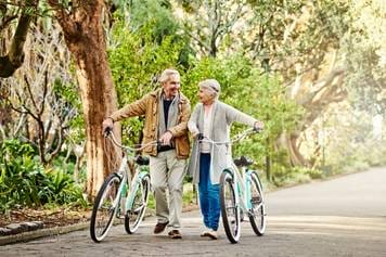 House of Hearing Richfield Utah - An older couple walking with their bicycles in a park.